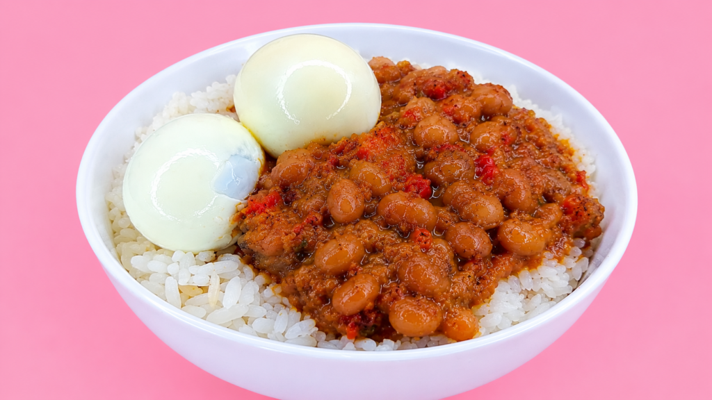 Nigerian white rice topped with stewed beans and two boiled eggs on a pink background.